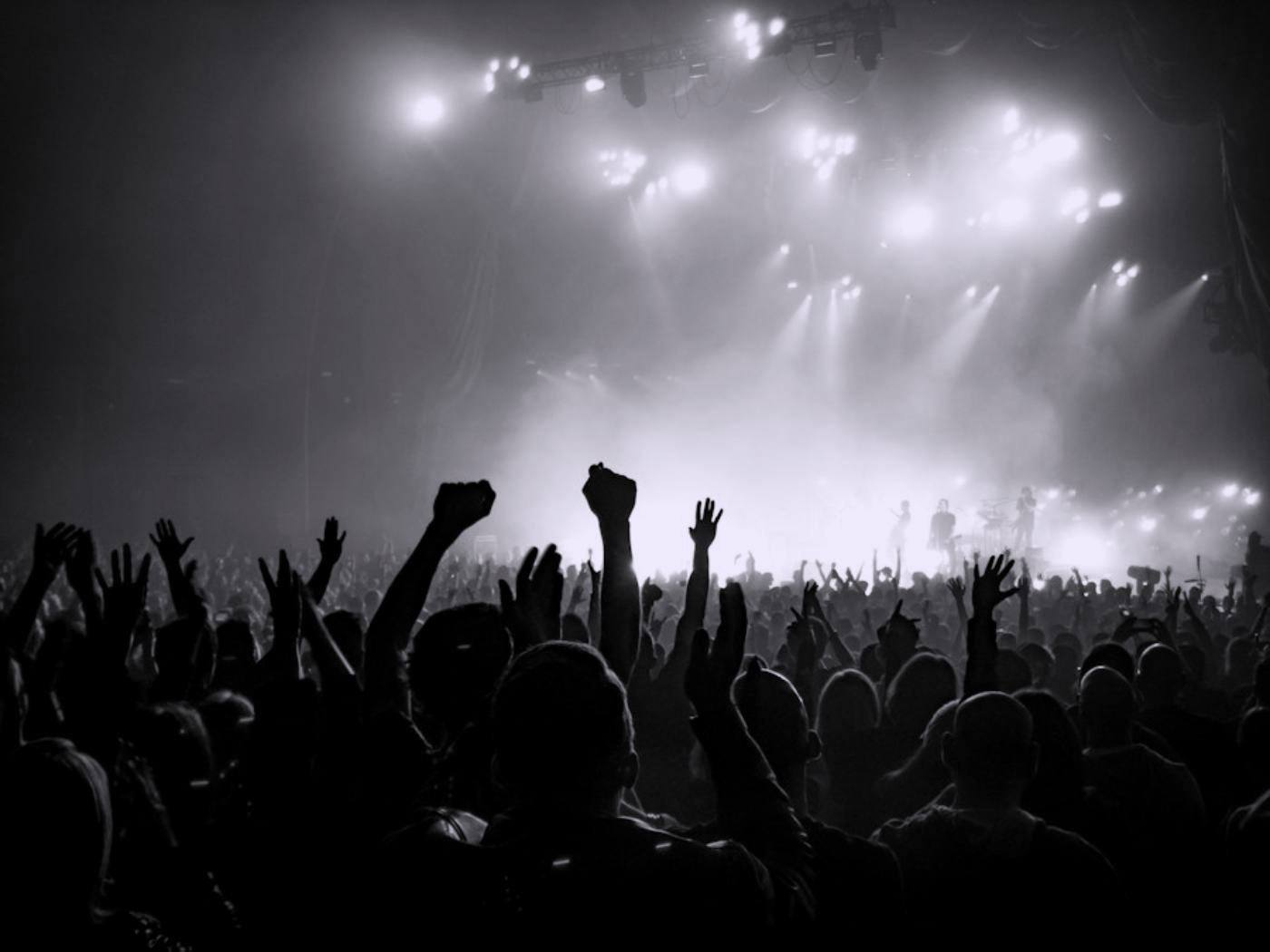 Stage lights cutting through haze above a crowd with raised hands.