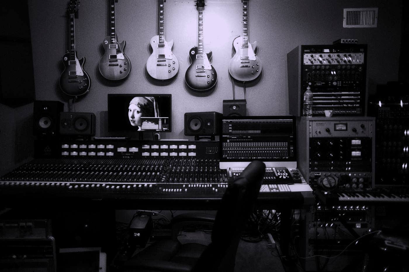 Guitars hanging above the mixing desk and outboard racks of a recording studio.