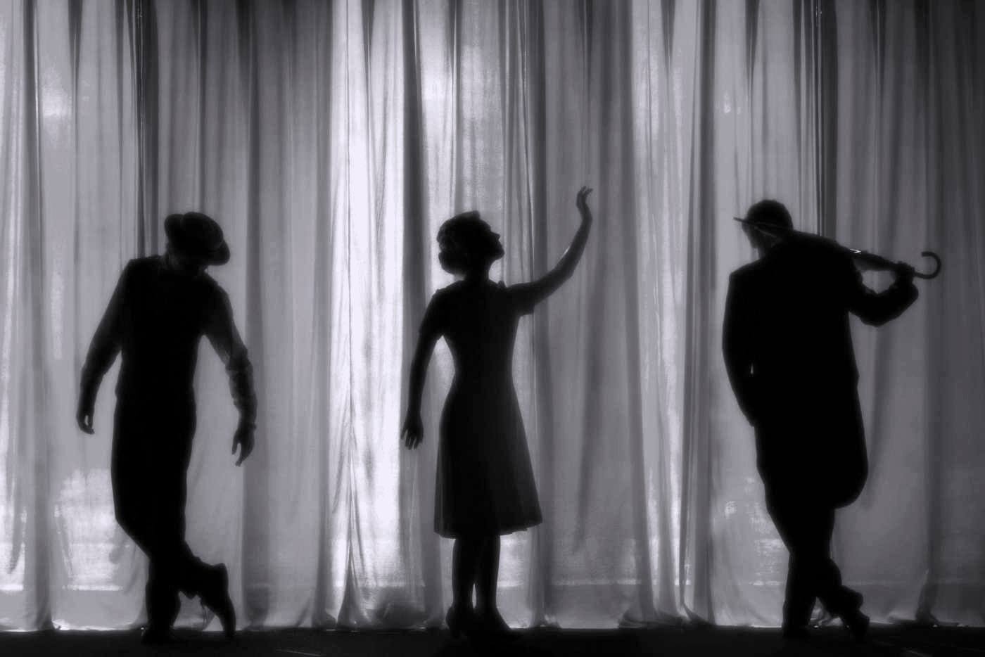 Three performers in silhouette against a lit stage curtain.